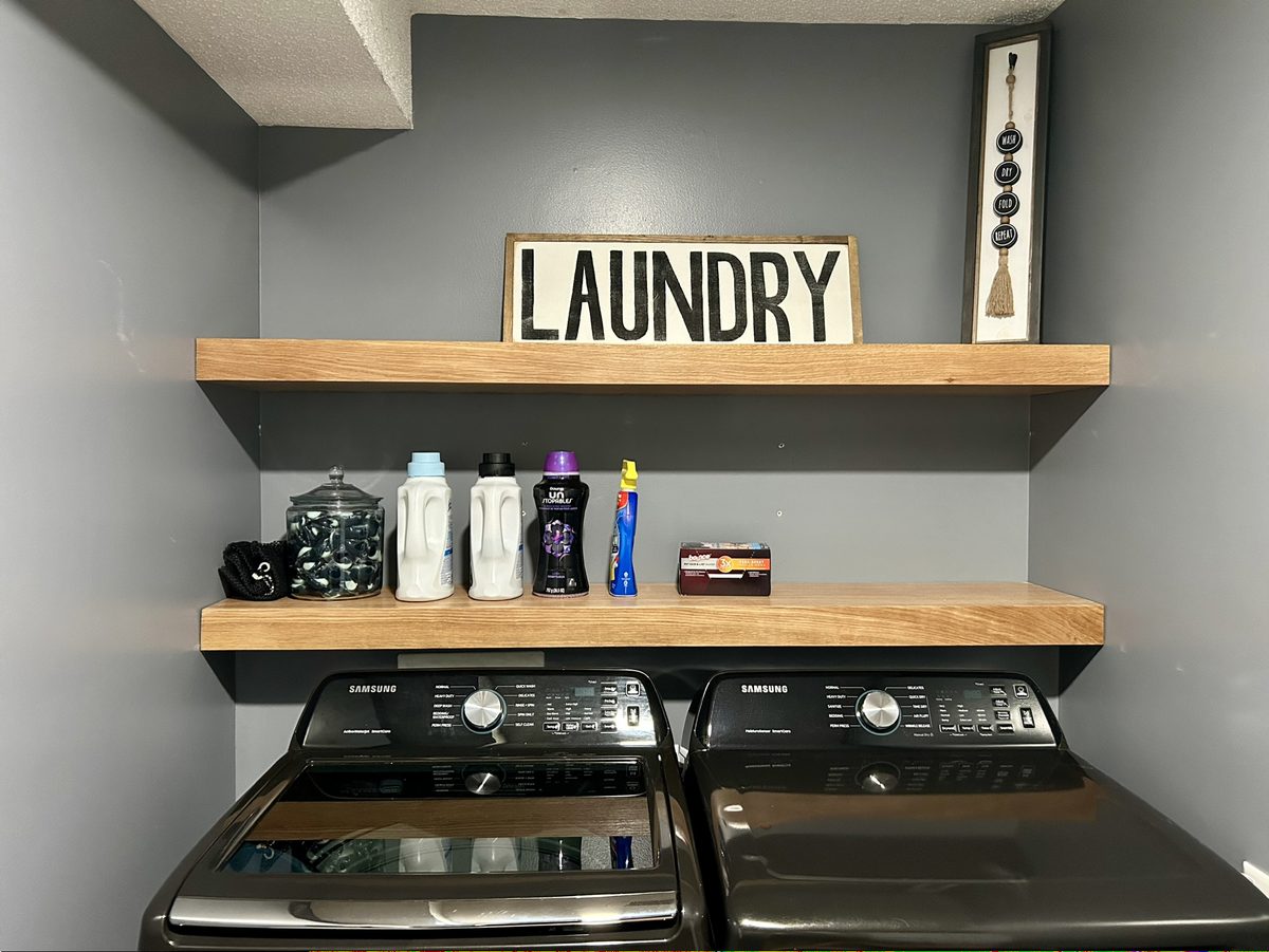 Two thick oak floating shelves fitted wall to wall above a washer and dryer