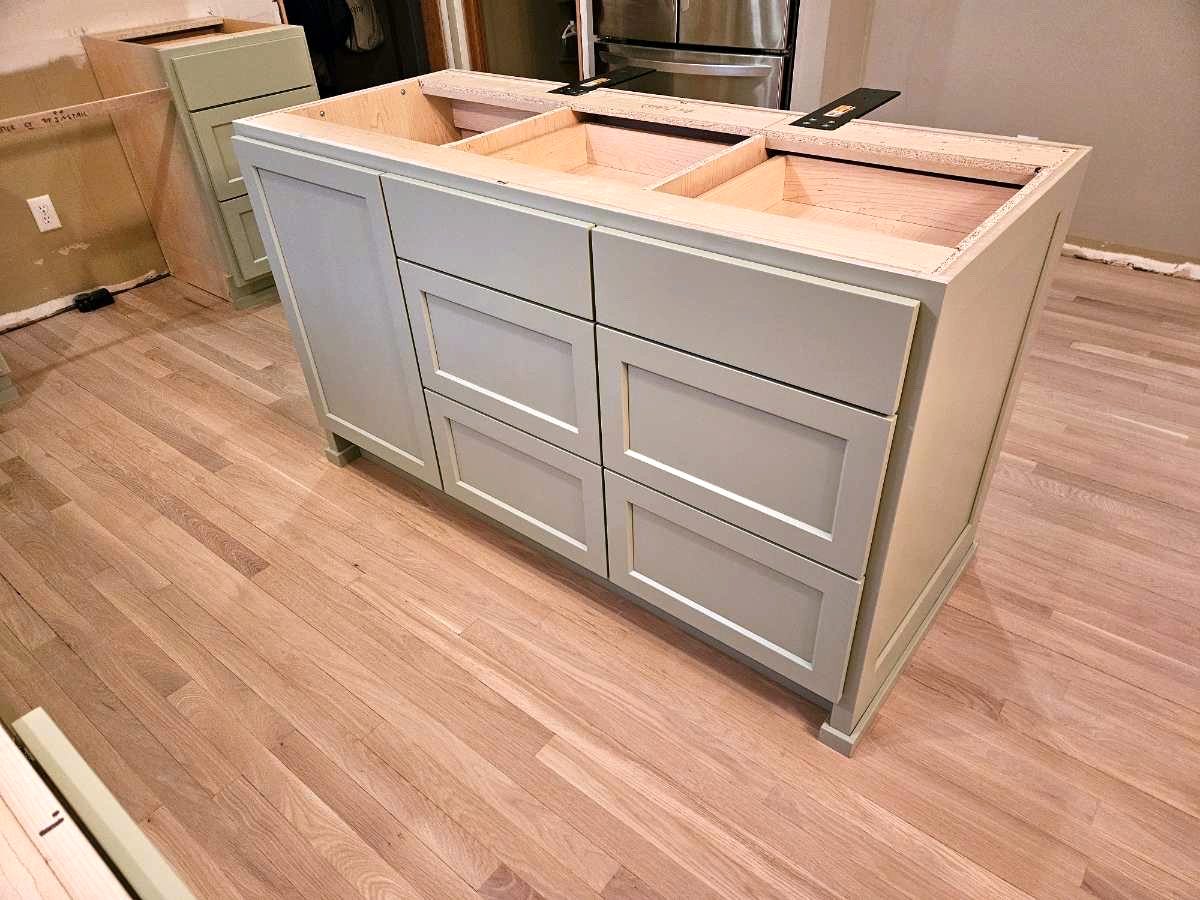 Sage green kitchen island with two drawer stacks, a paneled end and furniture-style feet