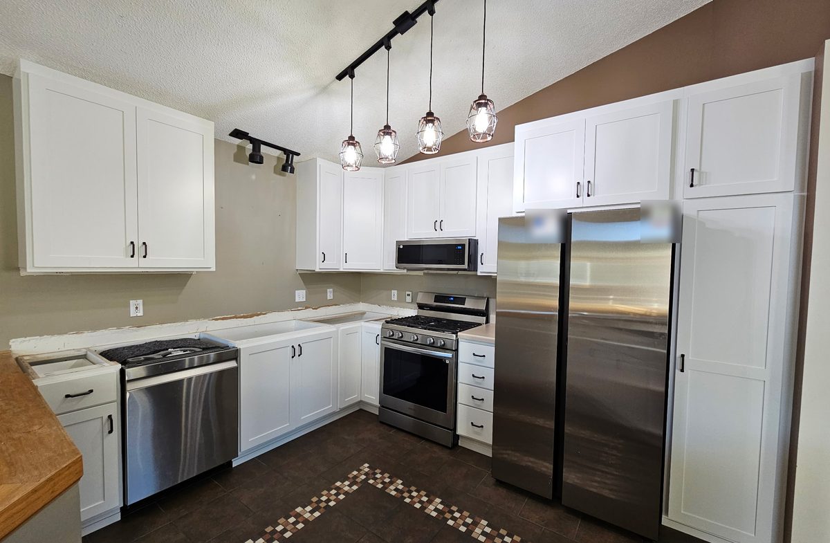 White shaker kitchen with matte black pulls, a refrigerator surround and a tall pantry under a vaulted ceiling