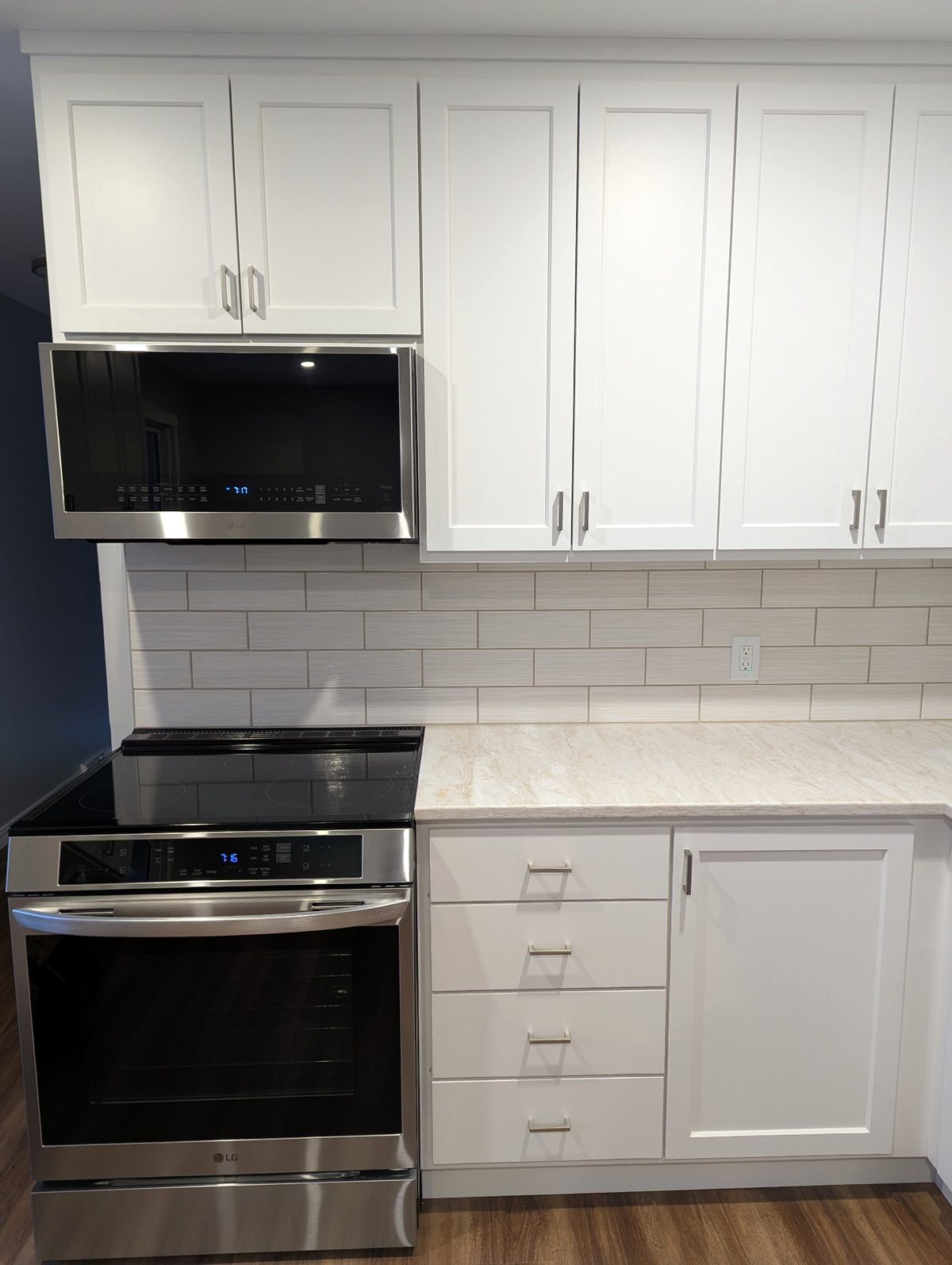 Four-drawer base cabinet and tall white shaker uppers beside the range and microwave