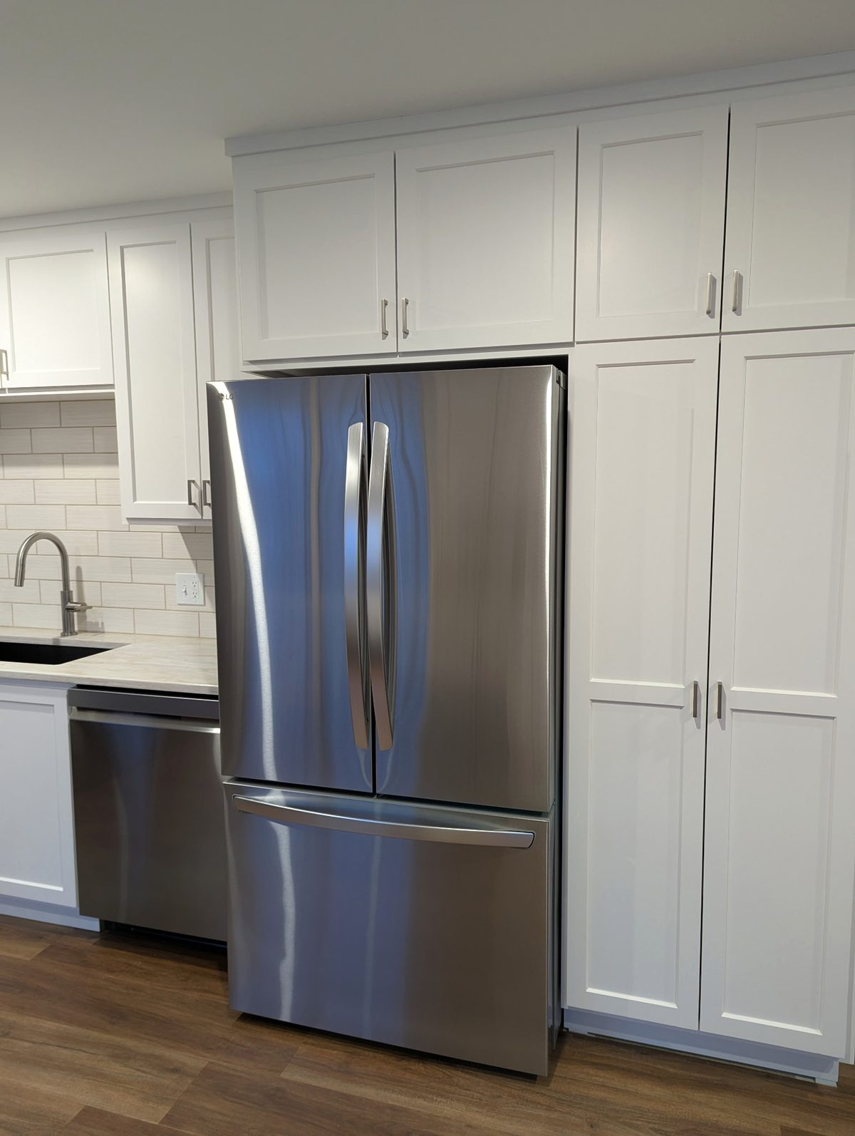 Refrigerator enclosure with a full-depth cabinet above and a tall two-door pantry in white shaker